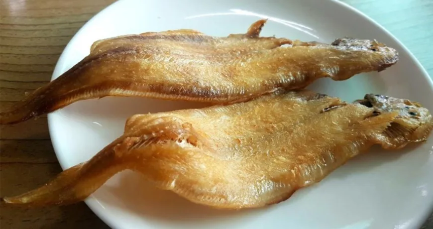 Close up of a grilled tongue sole fish dish. The skin appears crispy, and the flesh looks tender. The fish is centrally placed on a plate, with a blurred background that keeps the focus on the fish.